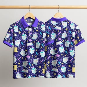 May include: Two short-sleeved polo shirts with a repeating pattern of whimsical ghost-like figures, books, feathers, and stars on a navy blue background. The shirts have purple collars and trim, hanging on a wooden hanger.
