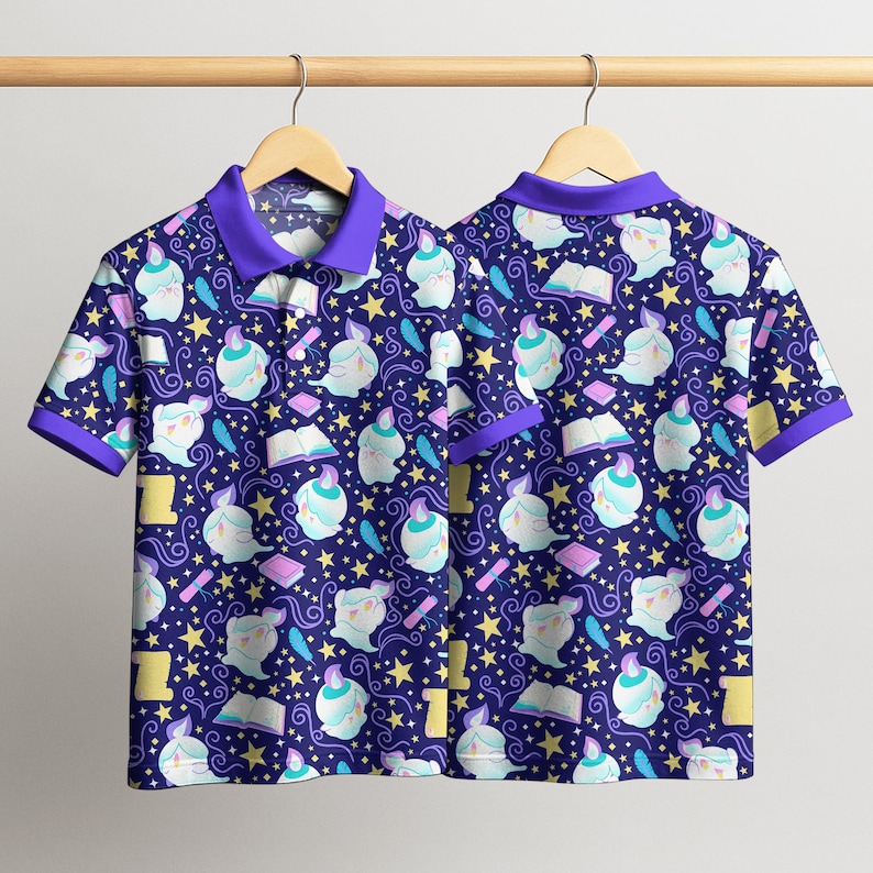 May include: Two short-sleeved polo shirts with a repeating pattern of whimsical ghost-like figures, books, feathers, and stars on a navy blue background. The shirts have purple collars and trim, hanging on a wooden hanger.
