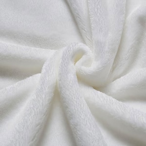 May include: A solid white plush fabric with a soft, fuzzy texture. The material is gathered in the center, creating deep, flowing folds and shadows that highlight the dense, velvety pile of the textile surface across the entire frame.