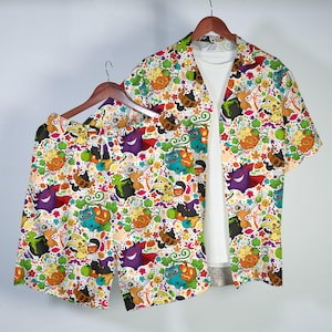 May include: A short-sleeve button-down shirt and matching shorts set featuring a colorful all-over print of various cartoon creatures, pumpkins, and autumn leaves. The shirt is worn over a plain white t-shirt, showcasing a vibrant Halloween theme.