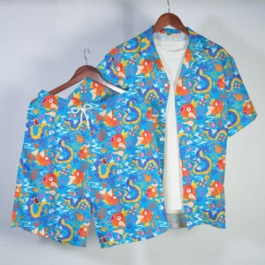 May include: A matching set of blue Hawaiian shirt and shorts with a vibrant pattern of orange and yellow cartoon fish and sea creatures. The shirt has short sleeves and a white undershirt. The shorts have a drawstring waist.