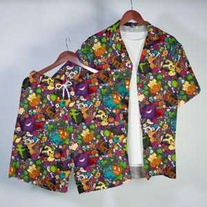 Könnte beinhalten: Ein Set aus einem kurzärmeligen Hemd mit Knopfleiste und passender Shorts, das mit einem bunten Muster aus verschiedenen Cartoon-Kreaturen, Kürbissen und grünen Kesseln auf dunkelviolettem Grund bedruckt ist. Das Hemd wird über einem weißen T-Shirt getragen.
