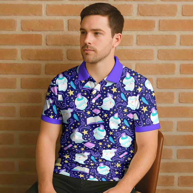 May include: A short-sleeved polo shirt with a whimsical pattern. The navy blue shirt features a repeating design of cartoon ghosts, books, stars, and feathers. The collar and sleeve trim are a solid purple color.