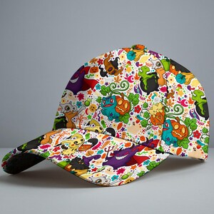 Op de afbeelding: Een baseballpet met een kleurrijke all-over print van diverse cartoonfiguren, pompoenen, groene ketels en herfstbladeren. Het ontwerp bevat paarse, oranje, groene en gele elementen op een witte achtergrond.