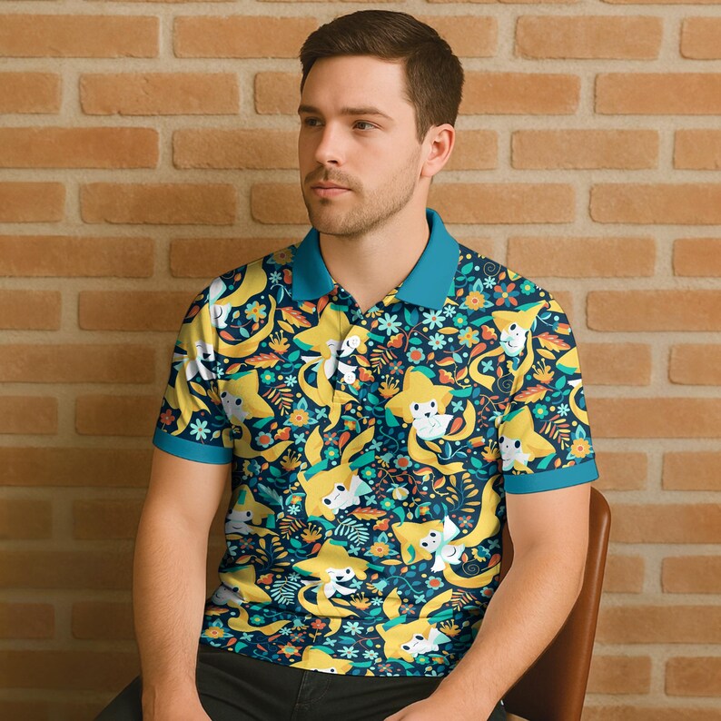 May include: A short-sleeved polo shirt with a vibrant pattern of yellow star-shaped characters, flowers, and leaves on a navy blue background. The shirt has a teal collar and sleeve trim. The person is sitting in a brown chair in front of a brick wall.