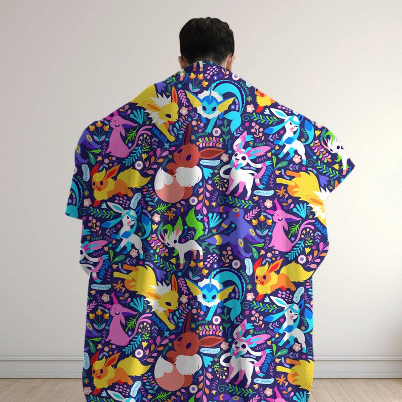 May include: A dark blue blanket featuring a repeating pattern of various colorful Eevee evolution characters interspersed with vibrant floral and leaf motifs in shades of pink, yellow, light blue, and green across the entire fabric surface.
