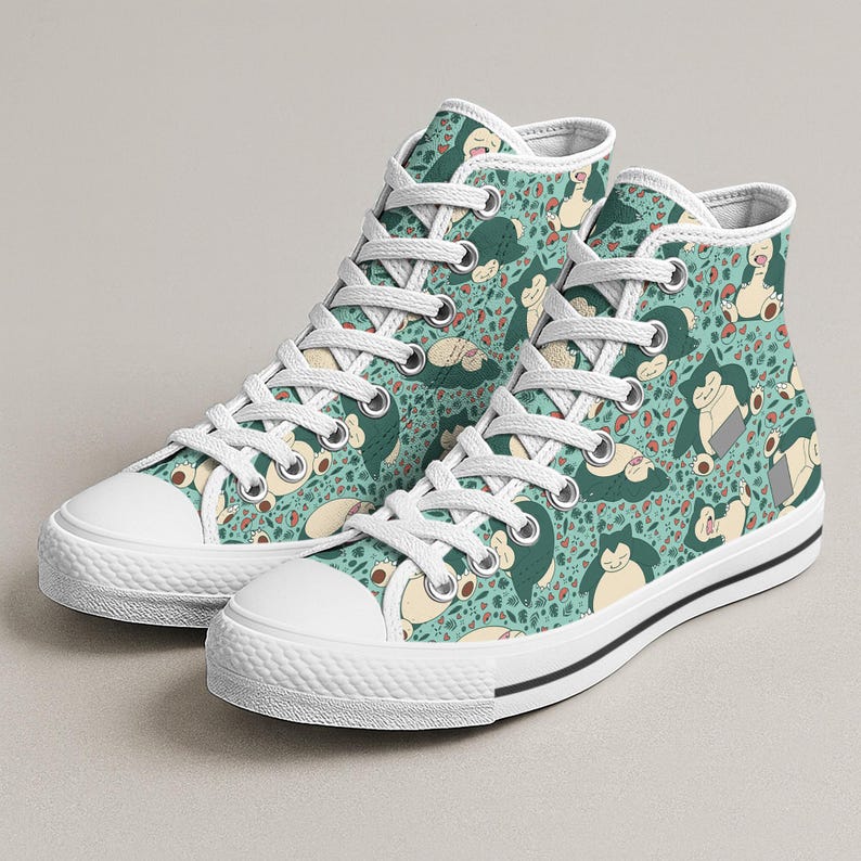 Op de afbeelding: Hoge canvas sneakers met een herhalend patroon van een stripfiguur op een turquoise achtergrond. De sneakers hebben witte veters, een witte neus en een zwarte streep langs de zool. Een leuk en speels ontwerp.