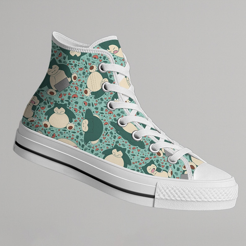 Op de afbeelding: Hoge canvas sneaker met een turquoise achtergrond met een herhaald patroon van stripfiguren, harten en andere kleine vormen. De sneaker heeft witte veters, een witte rubberen zool en een zwarte streep.