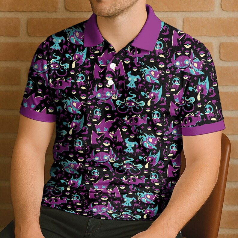 May include: Black polo shirt with a repeating pattern of purple, teal, and white cartoon characters. The shirt has a purple collar and sleeve trim. The design features various creatures and symbols on a black background.