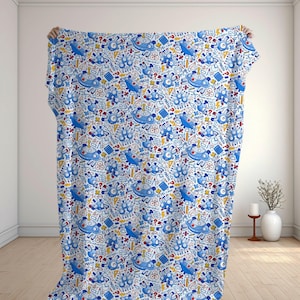 May include: A white throw blanket featuring a repeating pattern of blue robots, yellow geometric shapes, red question marks, and the word MATH printed in blue. The design includes various mathematical symbols and icons scattered across the fabric.
