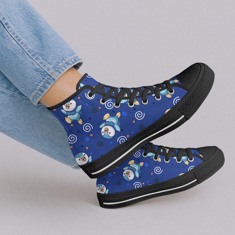 May include: Blue high-top sneakers with a repeating pattern of cartoon penguins, swirls, and dots. The sneakers have black soles, black laces, and a white stripe along the sole. The shoes are worn by a person wearing blue jeans.