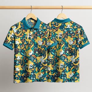 May include: Two short-sleeved polo shirts hanging on a wooden rack. The shirts feature a repeating pattern of yellow star-shaped characters with white faces, set against a dark teal background with floral and leaf accents. The collars and sleeve cuffs are teal.