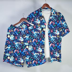 May include: A matching set of blue shorts and a short-sleeved button-up shirt with a white undershirt. The set features a repeating pattern of blue cartoon characters, sea creatures, and nautical elements on a dark blue background.