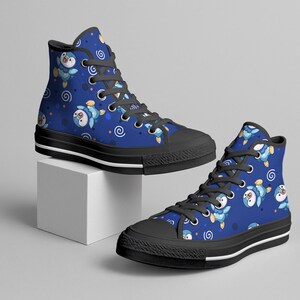 May include: High-top canvas sneakers with a blue background and a repeating pattern of cartoon penguins. The shoes have black soles, laces, and a white stripe along the bottom edge. The penguins are blue, white, and yellow.