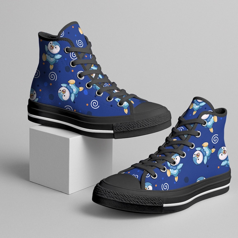 May include: High-top canvas sneakers with a blue background and a repeating pattern of cartoon penguins. The shoes have black soles, laces, and a white stripe along the bottom edge. The penguins are blue, white, and yellow.