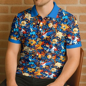 Puede incluir: Un polo azul con un estampado vibrante de personajes de dibujos animados multicolores. La camisa tiene cuello y ribetes de manga azules, y botones blancos. El dise&ntilde;o presenta una variedad de criaturas y elementos florales.