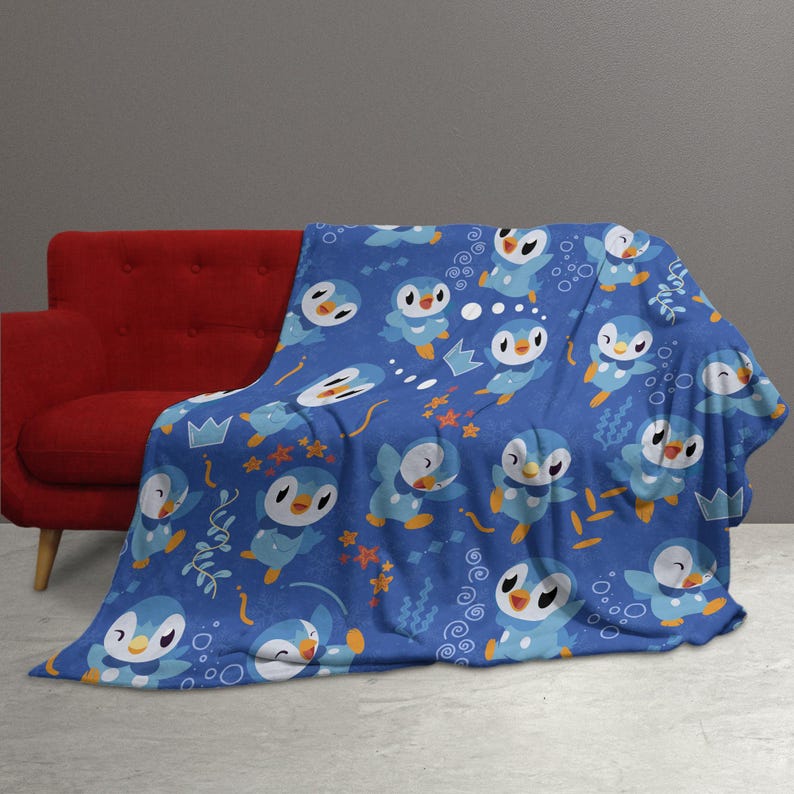 May include: A blue throw blanket featuring a repeating pattern of light blue and white penguin-like characters with yellow beaks and feet, interspersed with small orange starfish, light blue crowns, and white bubble motifs on a dark blue background.