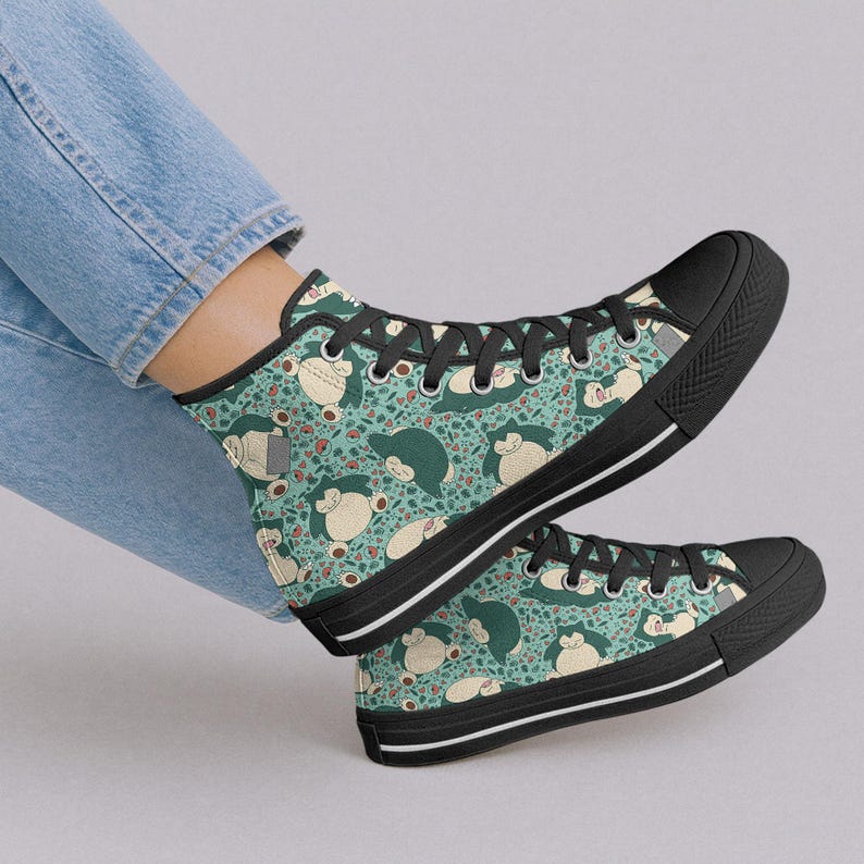 Op de afbeelding: Hoge canvas sneakers met een herhalend patroon van een stripfiguur op een turquoise achtergrond. De schoenen hebben zwarte zolen, zwarte veters en een witte streep langs de zool.