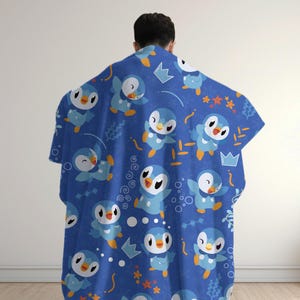 May include: A blue fleece blanket featuring a repeating pattern of cartoon penguins with light blue and white bodies, orange beaks, and feet. The design includes small orange starfish, white outlines of crowns, and various swirling line elements.