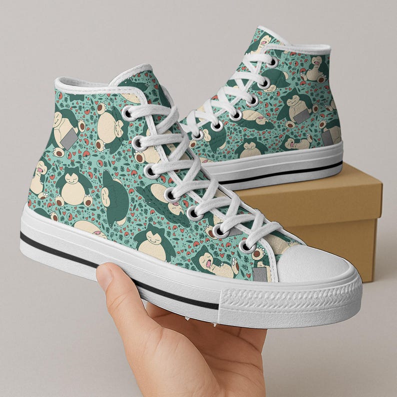 Op de afbeelding: Hoge canvas sneakers met een turquoise achtergrond en een herhaald patroon van een stripfiguur in verschillende poses. De sneakers hebben witte veters, een witte neus en een zwarte streep langs de zool.