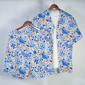 May include: A short-sleeve button-down shirt and matching shorts set featuring a white base with a repeating blue, red, and yellow pattern of cartoon magnets, calculators, geometric shapes, and the word MATH printed in a bold blue font.