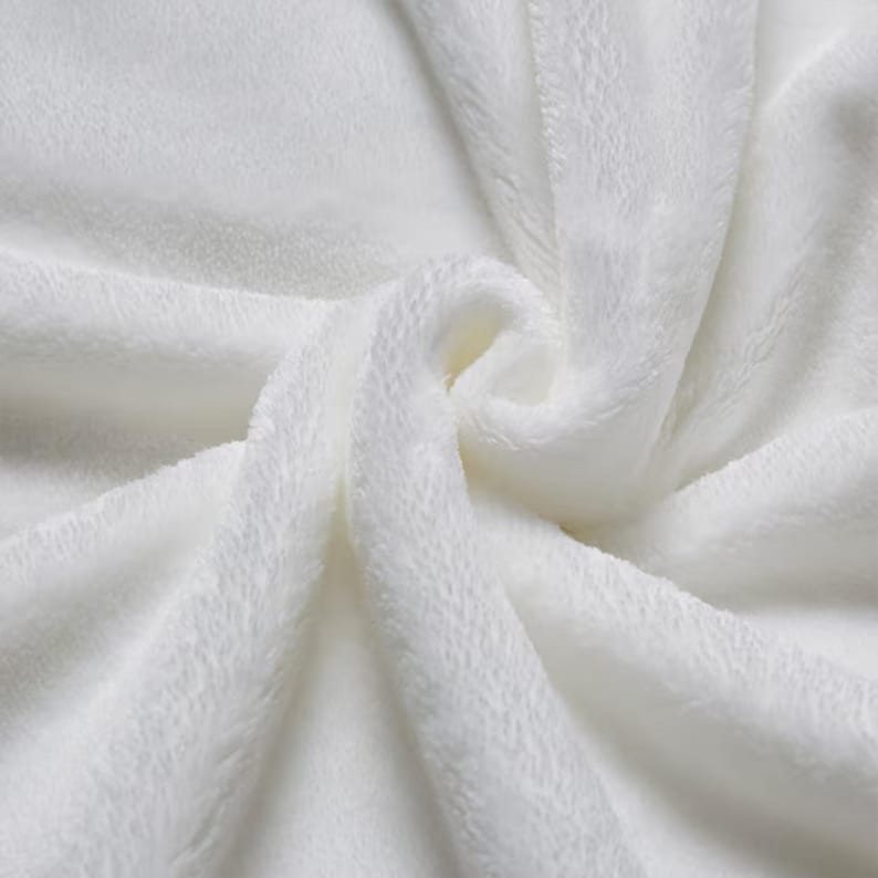 May include: A solid white fabric with a soft, plush, and fuzzy texture. The material is gathered in the center, creating deep, flowing folds and shadows that highlight the dense, velvety pile of the textile surface across the entire frame.