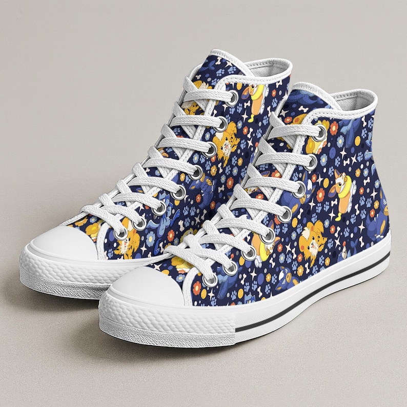 May include: High-top canvas sneakers with a navy blue background featuring a repeating pattern of cartoon dogs, paw prints, and flowers in yellow, orange, and blue. The sneakers have white laces, a white toe cap, and a black stripe on the sole.