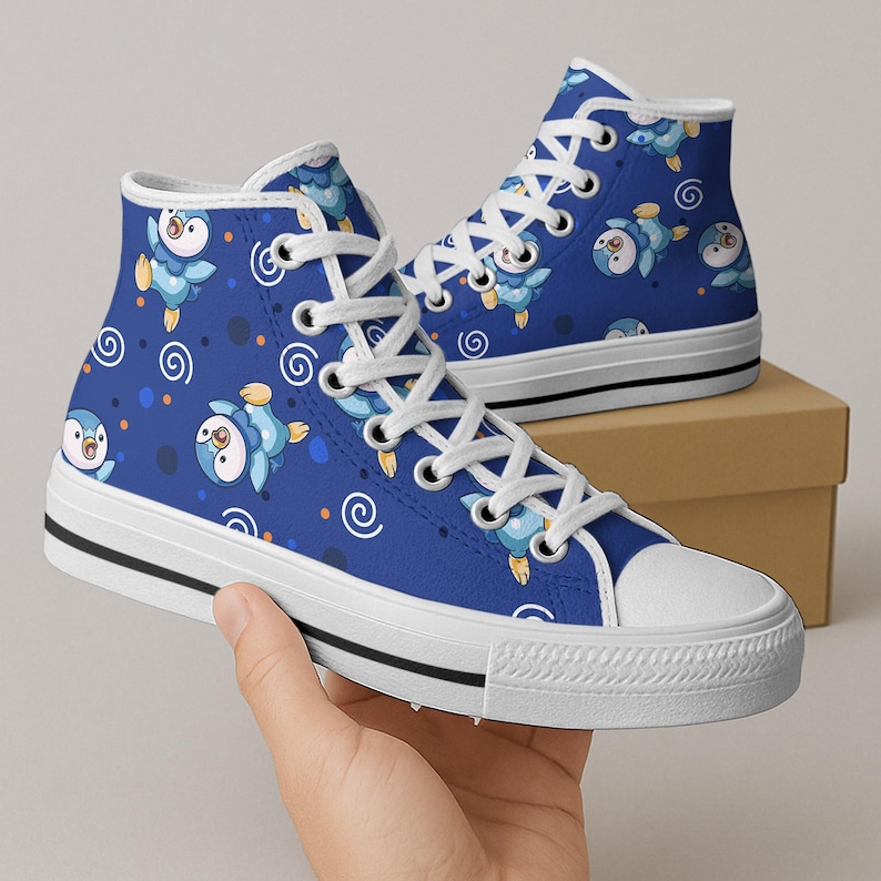 May include: High-top canvas sneakers with a vibrant blue background, adorned with a repeating pattern of cartoon penguins, spirals, and dots. The shoes have white laces, a white rubber toe cap, and a black stripe along the sole.