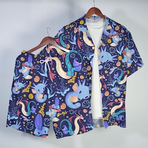 May include: A short-sleeved button-down shirt and matching shorts set in a dark blue fabric featuring a repeating pattern of light blue aquatic creatures, yellow swirls, and white seashells, worn over a plain white t-shirt.