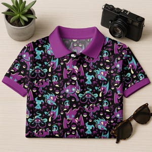May include: Black polo shirt with a purple collar and cuffs. The shirt features a repeating pattern of purple, teal, and white cartoon characters on a black background. A pair of sunglasses and a camera are next to the shirt.