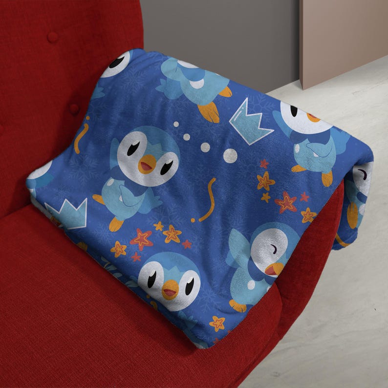 May include: A blue fleece blanket featuring a repeating pattern of light blue and white cartoon penguin characters with yellow beaks, interspersed with small orange star shapes, white crown outlines, and white snowflake motifs.