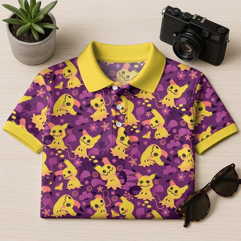 May include: A purple polo shirt with a yellow collar and cuffs. The shirt displays a repeating pattern of yellow cartoon characters, flowers, and leaves. It has three white buttons and is folded on a light wood surface.