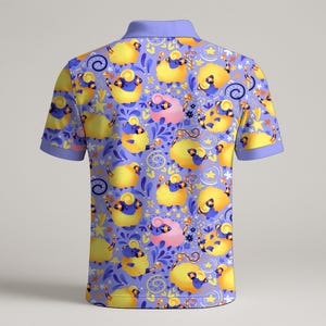 May include: A short-sleeved polo shirt with a whimsical pattern of yellow sheep with blue and pink accents on a lavender background. The shirt has a light purple collar and sleeve trim.