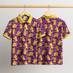 May include: A short-sleeved polo shirt featuring a repeating pattern of yellow cartoon characters on a purple background. The shirt has a yellow collar and sleeve trim. The shirt is hanging on a wooden hanger.