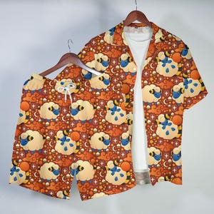 May include: An orange shorts and shirt set with a repeating pattern of cartoon sheep, moons, stars, and clouds. The short-sleeved shirt is open, revealing a white undershirt. The shorts have a drawstring.