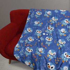 May include: A blue throw blanket featuring a repeating pattern of cartoon penguins with light blue bodies, white bellies, and orange feet. The design includes small orange starfish, light blue crowns, and white bubbles on a dark blue background.