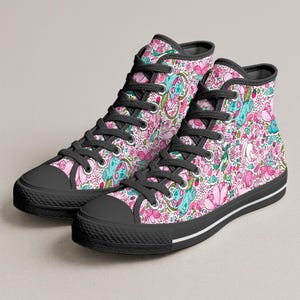 Puede incluir: Zapatillas de caña alta con un estampado vibrante sobre un fondo rosa claro. El patrón incluye criaturas de color verde azulado, flores de cerezo rosas, pequeñas hojas verdes y diversos alimentos. Los zapatos tienen cordones, punteras y suelas negras.