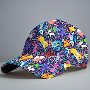 Op de afbeelding: Een baseballcap met een levendige all-over print met kleurrijke cartoonfiguren en bloemelementen op een donkerblauwe achtergrond. De cap heeft een gebogen klep en een gestructureerde kroon.
