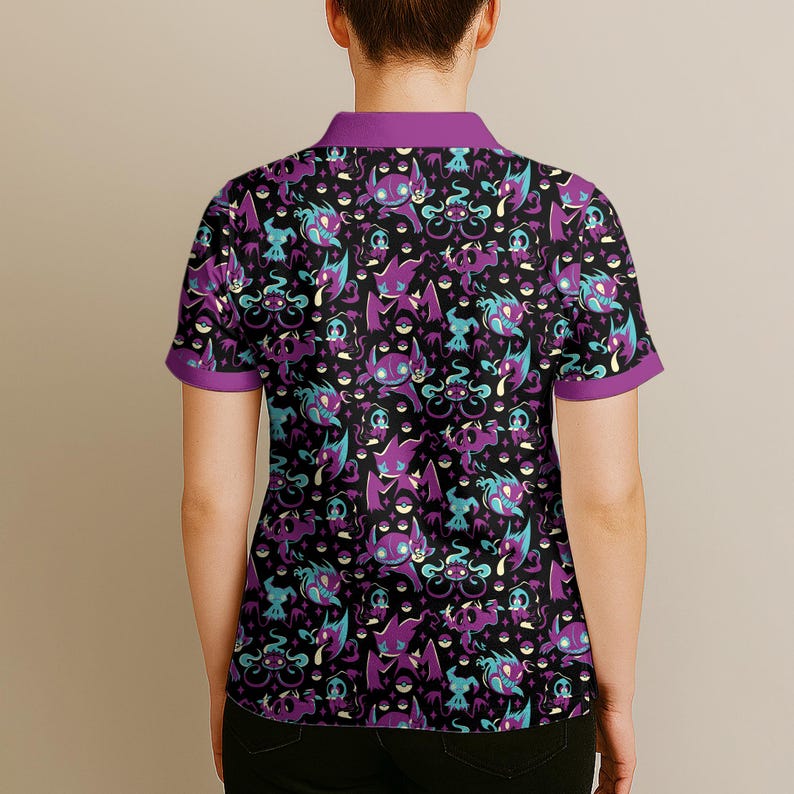 May include: Black polo shirt with a repeating pattern of purple, teal, and white cartoon characters. The shirt has a purple collar and sleeve trim. The design features various creatures on a black background.
