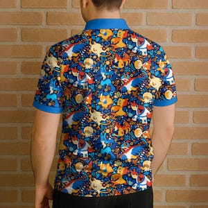 Puede incluir: Un polo azul con un estampado vibrante de personajes de dibujos animados en tonos azules, amarillos, naranjas y blancos. La camisa tiene cuello azul y mangas cortas con ribetes azules. El dise&ntilde;o est&aacute; sobre un fondo azul oscuro.