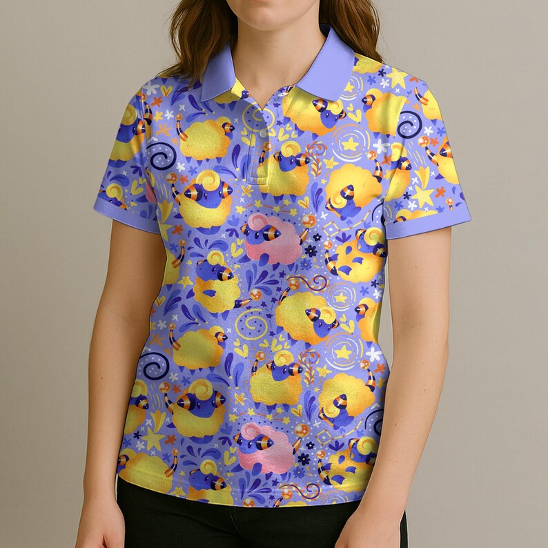 May include: A short-sleeved polo shirt with a whimsical pattern of yellow and pink sheep on a light purple background. The shirt has a light purple collar and sleeve trim. The sheep are interspersed with stars, flowers, and swirls.