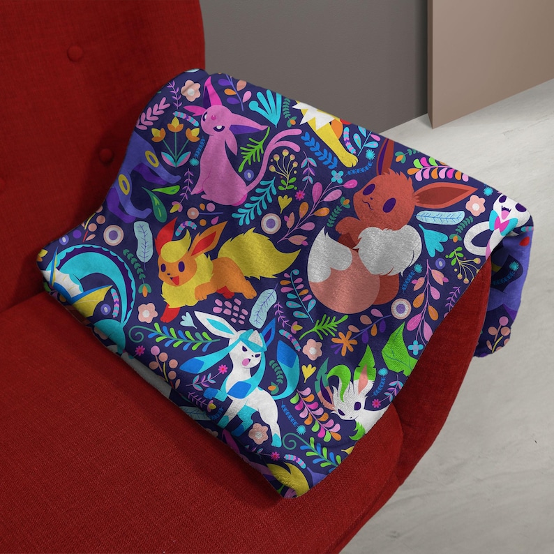 May include: A dark blue throw blanket featuring a repeating pattern of various colorful Eevee evolution characters, including Espeon, Flareon, Glaceon, and Leafeon, interspersed with vibrant floral and botanical elements in shades of pink, yellow, and green.