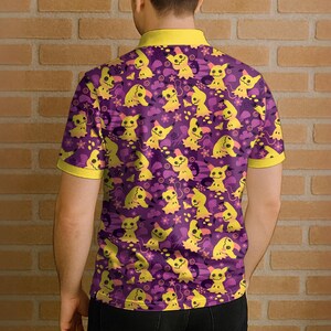 May include: Purple polo shirt featuring a repeating pattern of yellow cartoon characters and floral accents. The shirt has a yellow collar and sleeve trim. The design is set against a purple background.