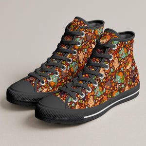 Puede incluir: Zapatillas de caña alta con fondo marrón oscuro y un patrón repetitivo de calabazas naranjas, flores pequeñas y varias criaturas de dibujos animados. Los zapatos tienen cordones negros, punteras de goma negra, suelas de goma negra con rayas blancas y ojales plateados.