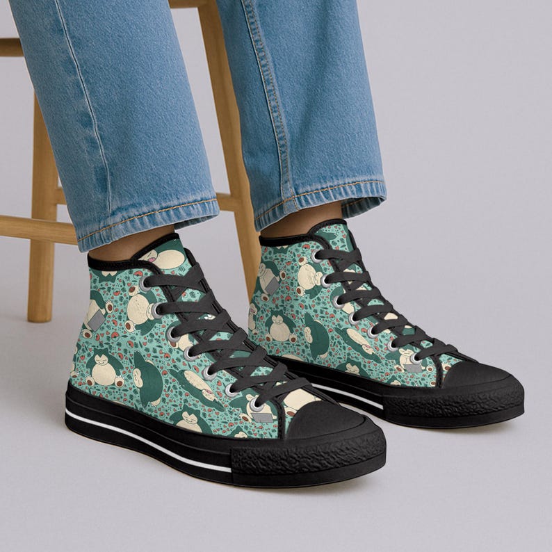 Op de afbeelding: Hoge sneakers met een teal achtergrond en een herhalend patroon van een stripfiguur in wit, beige en donkergroen. De sneakers hebben zwarte veters, een zwarte neus en een zwarte zool met een witte streep.