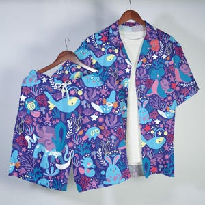 May include: A matching set of clothing, including a short-sleeved button-down shirt and shorts, both featuring a vibrant, colorful underwater-themed pattern. The design includes various sea creatures and aquatic plants on a purple background.