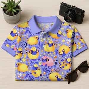 May include: A short-sleeved polo shirt with a whimsical sheep pattern in yellow, blue, and pink on a lavender background. The shirt has a light blue collar and cuffs. A camera and sunglasses are next to the shirt.