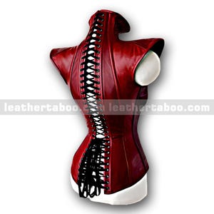 Pu&ograve; includere: Un corsetto in pelle bordeaux con lacci neri sulla schiena. Il corsetto ha un colletto alto e spalle strutturate. Il testo "leathertaboo.com" &egrave; stampato in basso a sinistra e a destra dell'immagine.