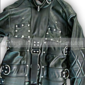 Könnte beinhalten: Schwarze Lederjacke mit mehreren Riemen, Metallringen und silbernen Nieten. Die Jacke hat einen hohen Kragen und eine Steppung an den Ärmeln. Das Design umfasst mehrere Riemen mit Schnallen und D-Ringen.