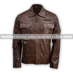 May include: A dark brown leather jacket featuring a central brass-toned zip, a pointed collar, and multiple utility pockets on the chest and sleeves. The garment includes horizontal flap pockets and a small zipped pocket on the upper left chest.